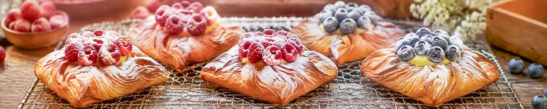 Freshly baked pastries topped with raspberries and blueberries, cooling on a rack