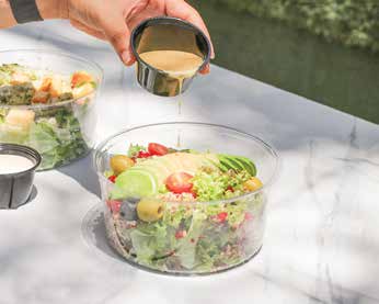 A fresh salad bowl with cherry tomatoes, olives and avocado being dressed
